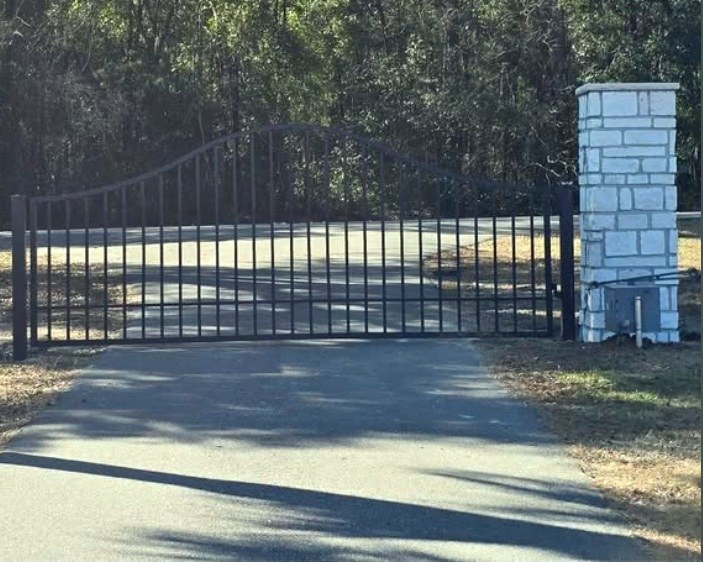 Black driveway gate with stone columns